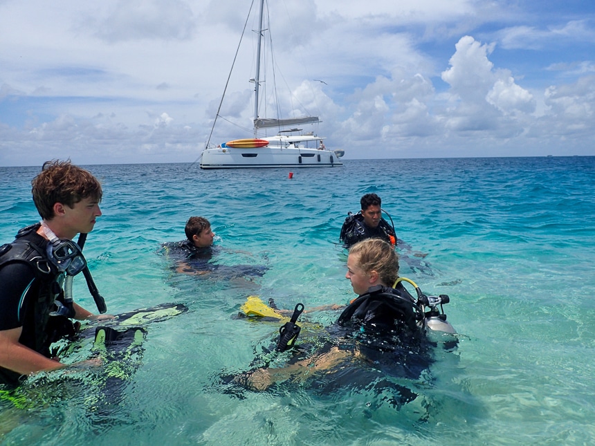 In Belize a group of scuba divers float in shallow water during their training in front of their private catamaran charter boat