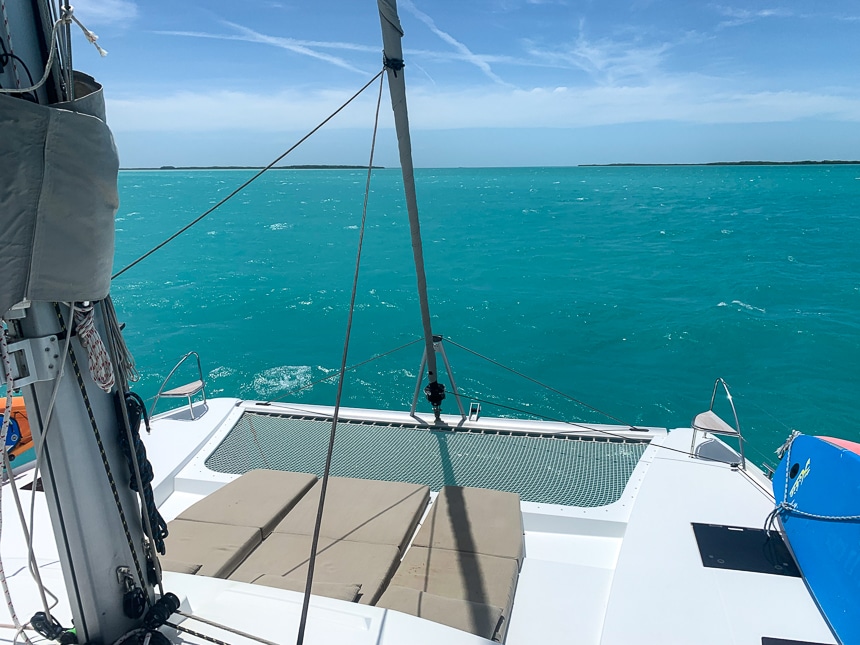 Looking over teal ocean water and blue sky from the back of a white Belize catamaran with three lounge mats and a netted trampoline.