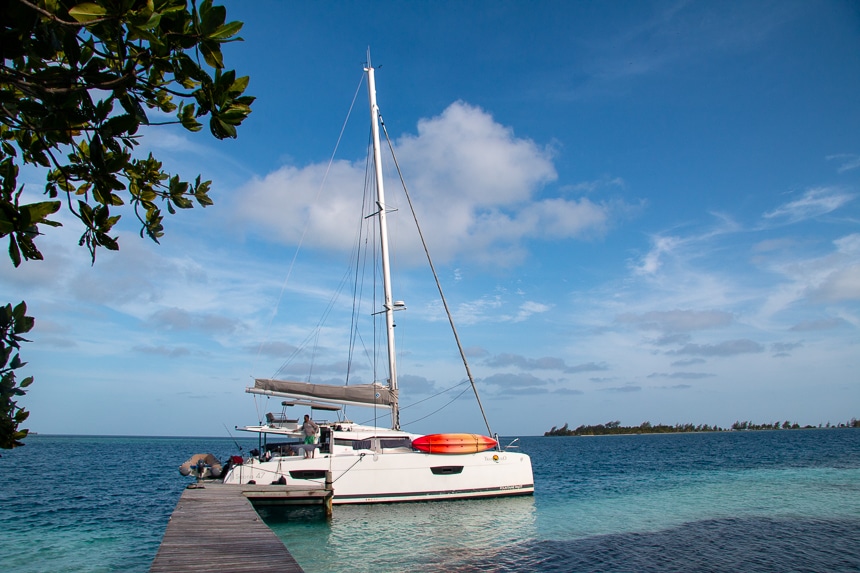 A wooden dock stretches into the teal blue ocean water of Belize, a bright while sailboat floats at the end waiting for its guests.