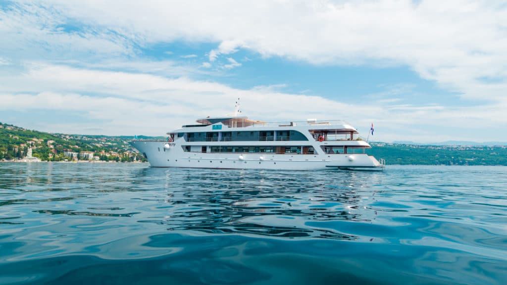 A luxury yacht charter in the Mediterranean Sea seen at sea level with blue water in foreground and green hills in background