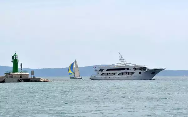 A Mediterranean yacht charter boat seen cruising beside a sailboat and a lighthouse