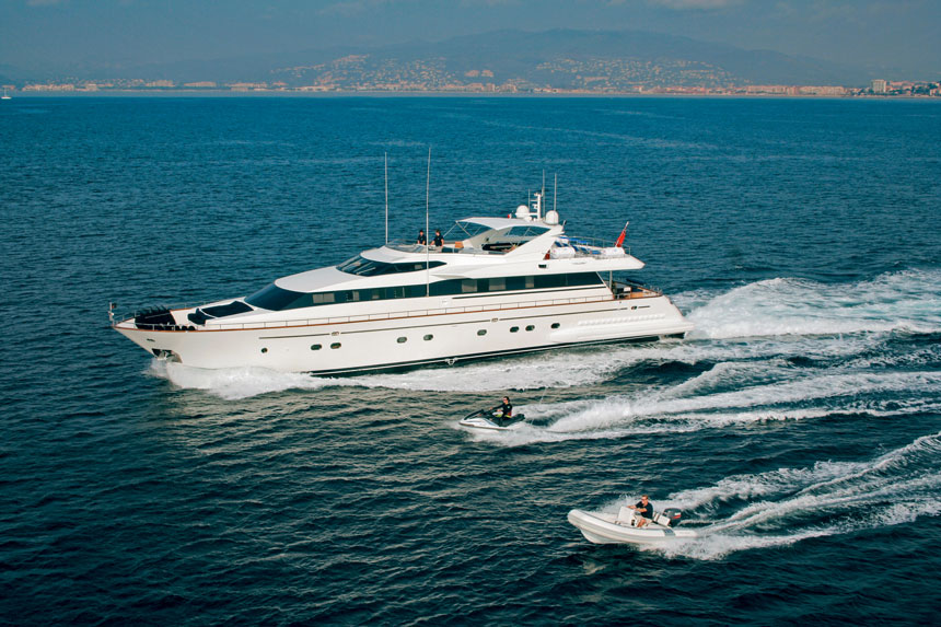 Private white yacht cruises in open Mediterranean waters with jet ski & tender cruising beside.