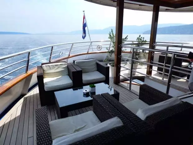 Small ship motor yacht Futura stern side with lounge chairs and tables outside on the deck.