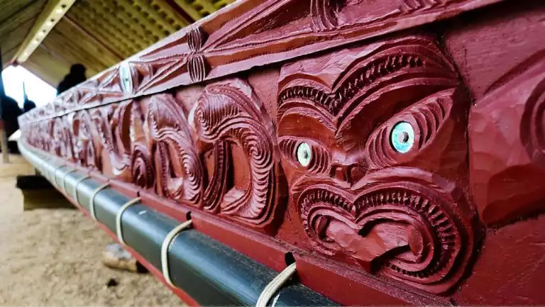 Red wood carving shows Maori spirits with bright blue eyes, seen on the National Geographic New Zealand Cruise.