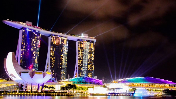 Singapore downtown buildings and statues lit up at night in purple, pink & teal, seen on a cruise from Singapore to Bali.