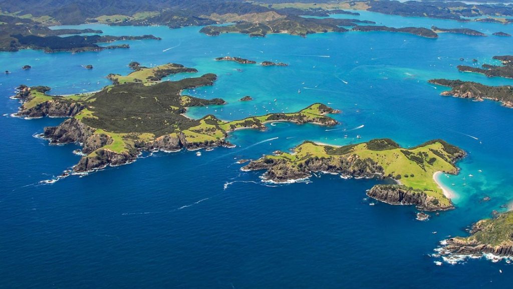 Aerial view of bright green islands among deep blue & turquoise sea, seen on the National Geographic New Zealand Cruise.