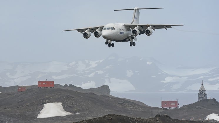 A plane lands at Frei Station with red buildings for an Antarctica air cruise