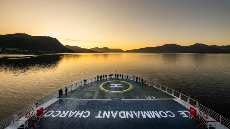 Aerial view of Le Commandant Charcot expedition ship's bow with travelers standing on the heli pad watching the sunrise.