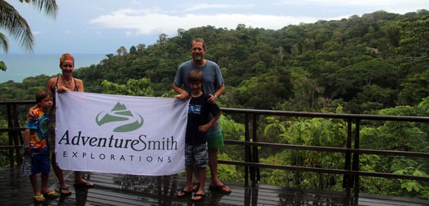 Costa Rican traveling family holding the Adventuresmith Explorations flag on the deck overlooking jungle and ocean in Lapa Rios.