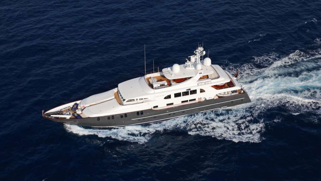 Aerial view of superyacht in Galapagos Aqua Mare cruising at speed in calm water, with blue hull, teak decks & white upper decks.