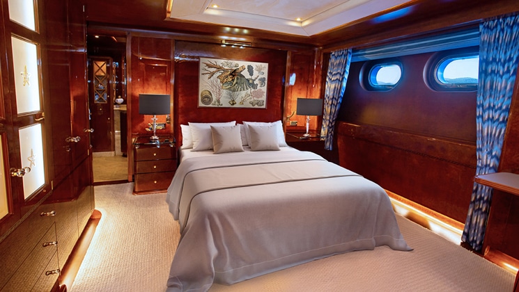 Category III cabin on Aqua Mare Galapagos superyacht with queen bed, wooden walls, portholes, accent lights & nautical theme.