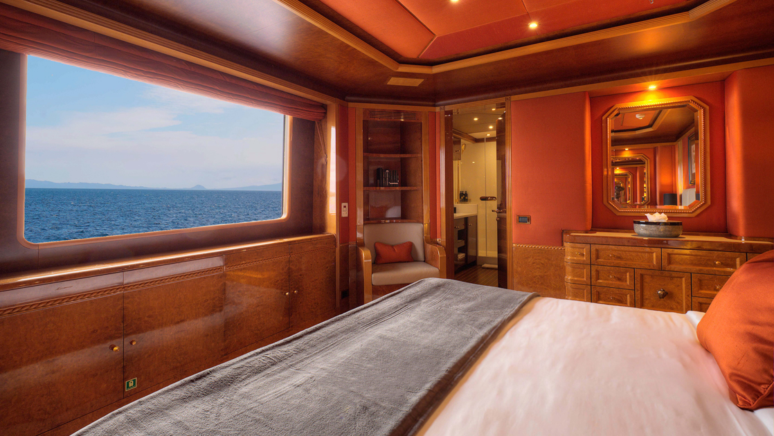 Category II cabin on Aqua Mare Galapagos superyacht with queen bed, red & wood walls & large view window.
