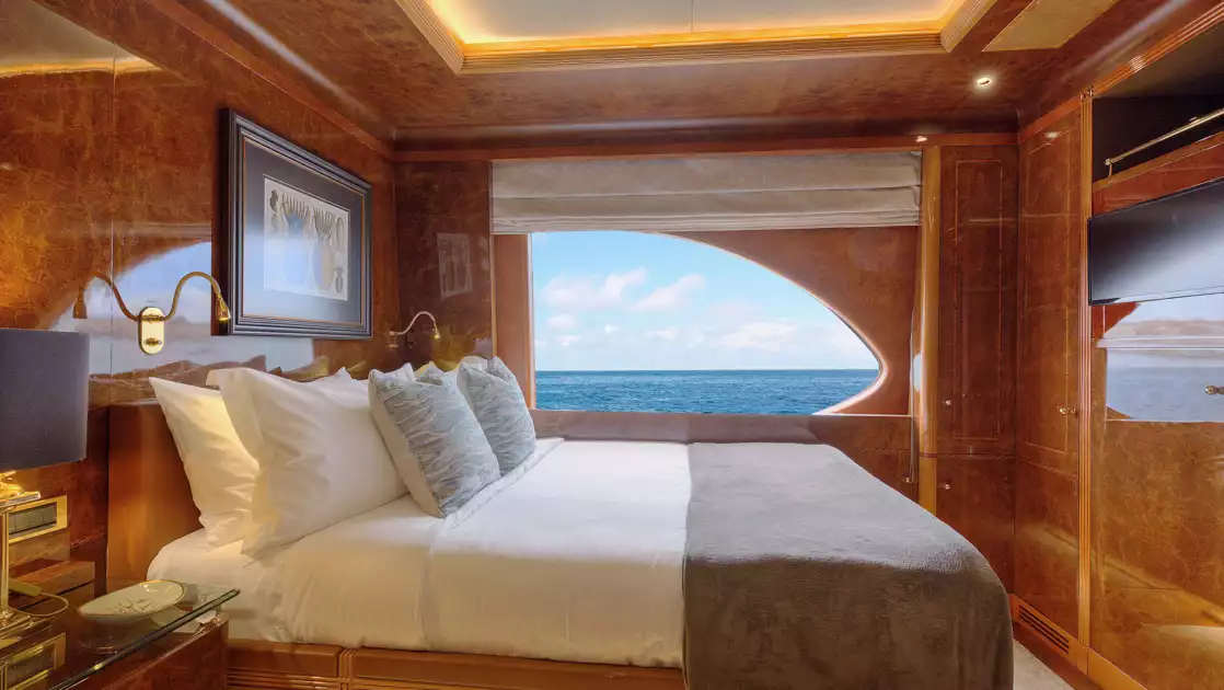 Category V cabin on Aqua Mare Galapagos superyacht with queen bed, wooden walls, view window, accent lights & nautical theme.