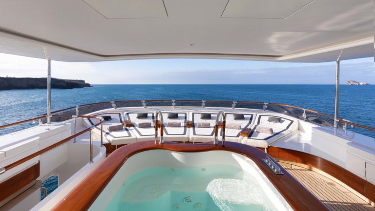 Covered Sun deck Jacuzzi of veneer, white & teak on Aqua Mare Galapagos superyacht, with blue & white chaise loungers.