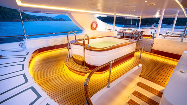 Covered Sun deck Jacuzzi of veneer, white & teak on Aqua Mare Galapagos superyacht, with accent lights & adjacent stairway.
