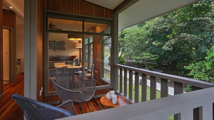 Outdoor deck with 2 chairs overlooking cloud forest at Hotel Senda Monteverde & glass windows looking into suite interior.