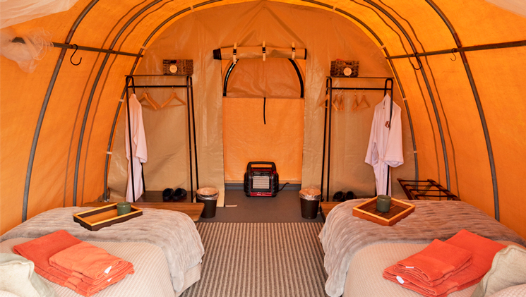 Tunnel-style canvas tent at Bear Camp Alaska with 2 twin beds, luxury bedding, 2 white robes, space heater & clothes racks.