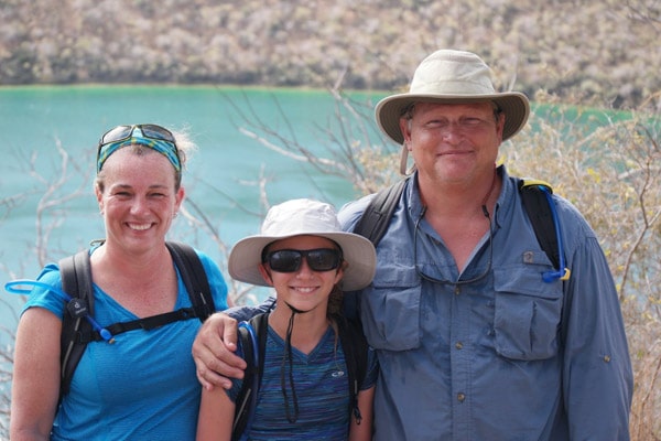 A mother, father and daughter in expedition gear, backpacks and blue shirts pictured ashore on a Galapagos family cruise.