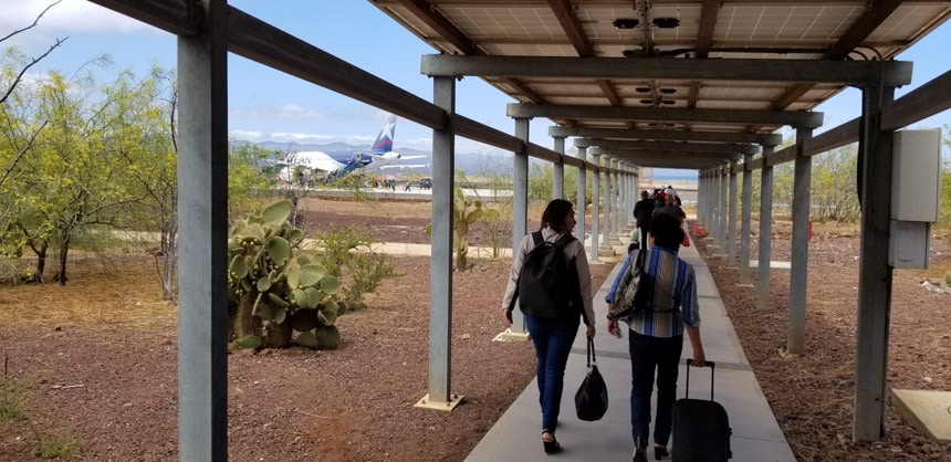 Two travelers walk under an awning toward a plane in the distance at the Galapagos airport on Baltra Island