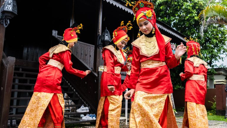 Traditional house & dance performance by 4 women in red & gold dresses, in Pulao Belitung, Indonesia.