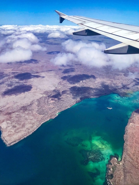 Photo from the Galapagos airplane window, looking over the airplane wing down at and the crystal teal blue ocean water surrounding the islands below. 