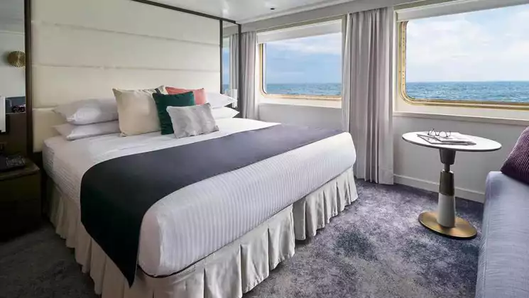 Suite aboard National Geographic Islander II Galapagos ship with double bed, large view windows & white & blue decor.