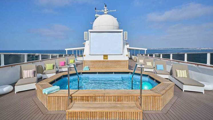 Sun Deck on Nat Geo Islander II ship in Galapagos with large Jacuzzi & many gray chaise loungers with colored throw pillows.