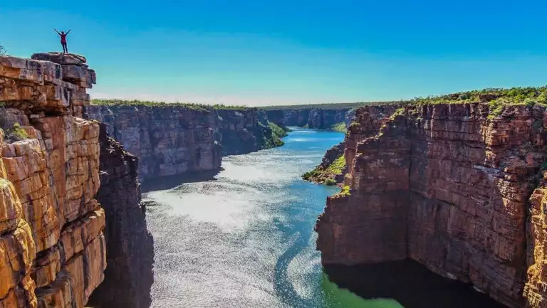 Australia traveler stands atop a cliff edge high above a large river between red rock walls on a Nat Geo Kimberley Expedition.