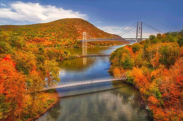 The Hudson River with two bridges and forest foliage with fall colors and blue sky above. 