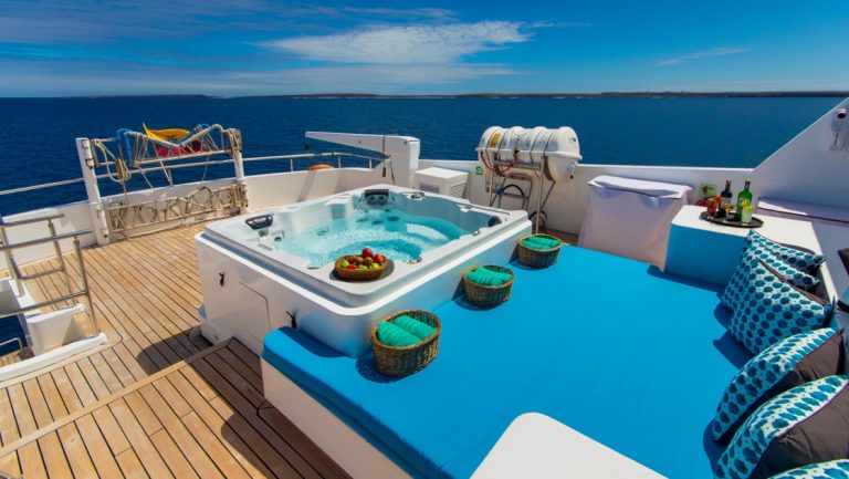 Sun Deck of Grand Majestic motor yacht with Jacuzzi beside large sun bed with bright blue padding & pillows, cocktails & towels.