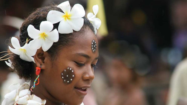 Girl with white flowers & native paint on her face gazes downward during a cultural presentation on a South Pacific cruise.