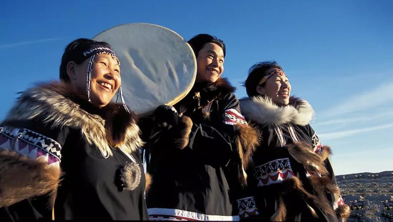 Three Inuit women, arctic indigenous people of Greenland, dressed in traditional clothing and hold a musical instrument.
