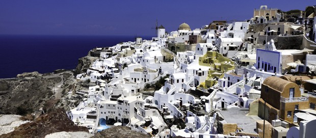 The Greek island of Santorini with white buildings and structures blanketing a hillside.
