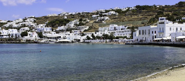 The Greek town of Mykonos from the shoreline with white structures scattered through out a hillside.