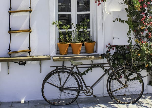 White buiding wall with window rope ladder, bougainvillea, potted plants and old townie bike.