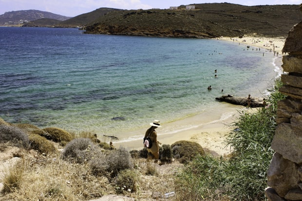 Traveler hiking down to white sandy beach in Greece.