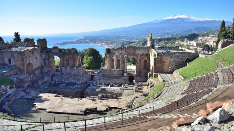 A colloseum seen from the top seats with the ocean and a snow-capped volcano in the distance