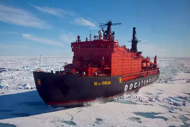 Russian icebreaker 50 Years Of Victory pushing through sea ice. Black hull and bright red square decks with windows.