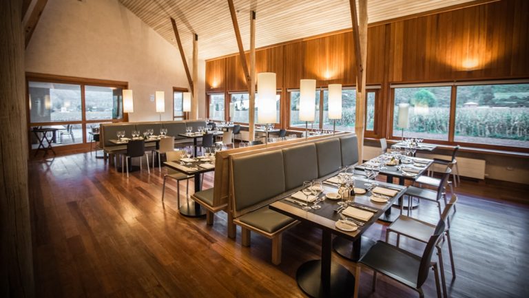 Dining room at Explora Sacred Valley Lodge with 2 rows of booth seating & chairs opposite under a high ceiling & by large windows,