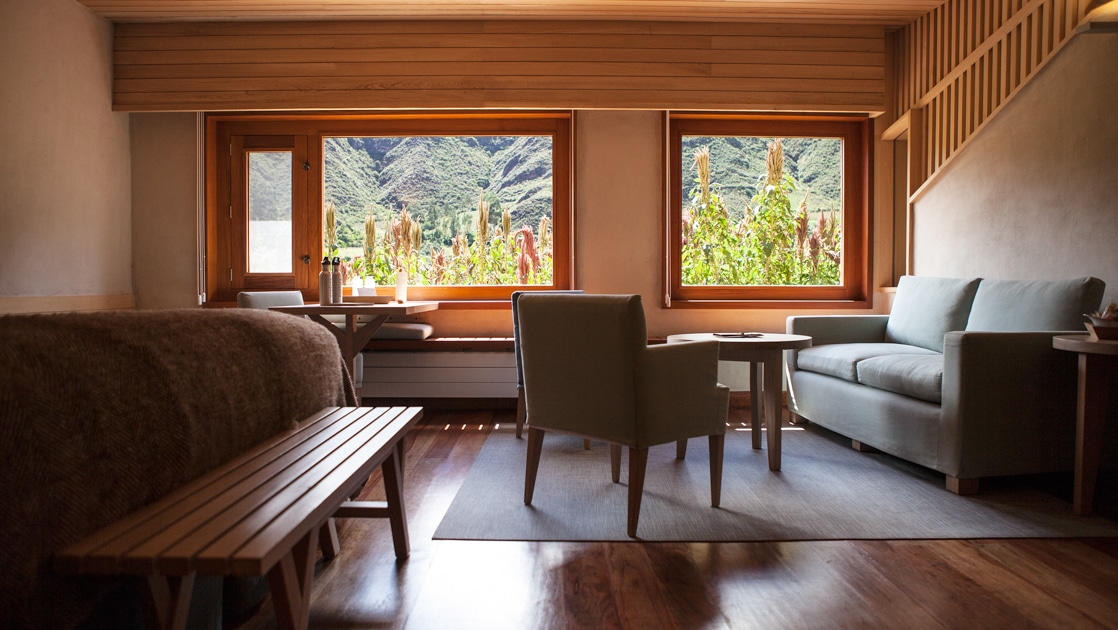 Suite at Explora Sacred Valley lodge Peru with beds large window, exterior door, couch, table & 2 chairs in a minimalist decor.