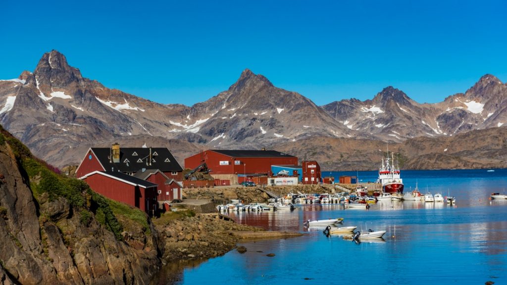 Tasiilaq, a town in Arctic southeastern Greenland with bright red wooden buildings and harbor surrounded by high mountains.