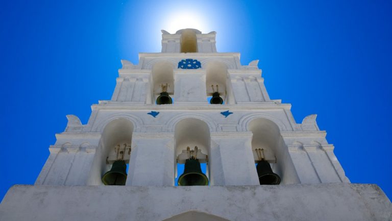 Looking up at a 3-tiered set of church bells amongst white pillars, seen on the At The Heart of The Greek Islands voyage.
