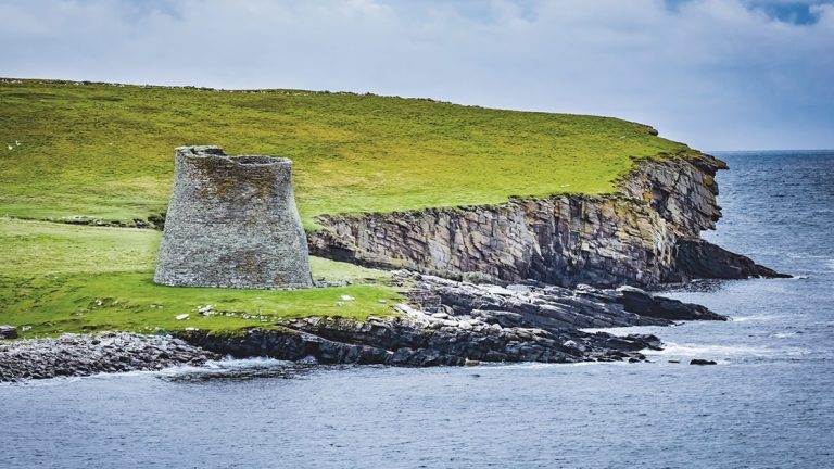 Mousa Broch seen among green grass waterfront on Mousa island in Shetland, Scotland, is the finest preserved example of an Iron Age broch or round tower.