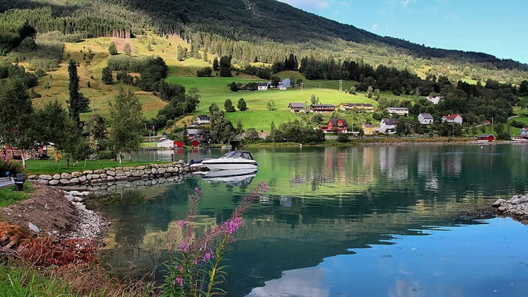 Small white day boat sits docked in glassy water beside rolling green hills during a Norwegian fjords cruise.