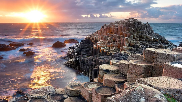 Sunset over the sea by tan circular rock columns on shore, seen on the Treasures of Ireland & The British Archipelagoes trip.
