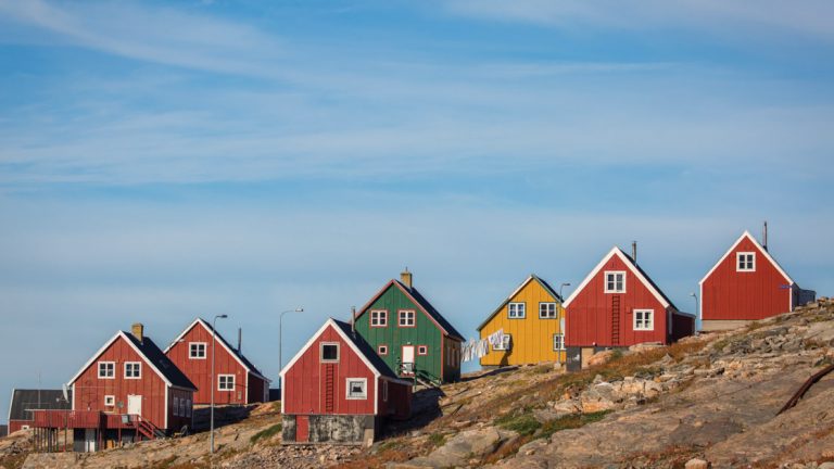 Seven brightly colored red, green and yellow houses seen on a rocky hill in Ittoqqortoormiit Greenland.