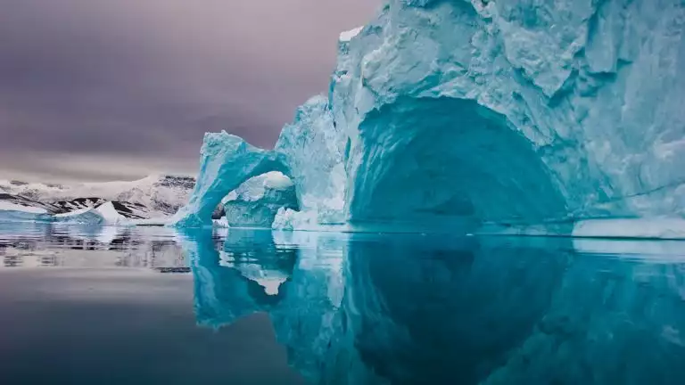 A giant blue iceberg with a cave indention & arch feature seen among still water