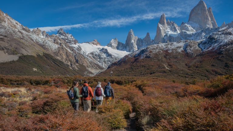 Explora El Chalten guests walk through autumnal valley under a blue sky en route to tall jagged peaks in the distance.