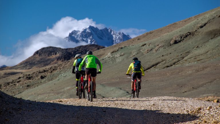 3 Explora Patagonia National Park travelers in bright green & yellow jackets ride mountain bikes uphill on a gravel road.