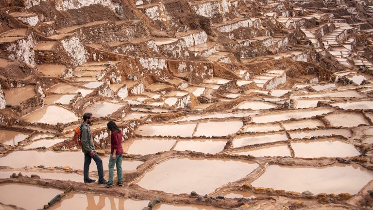 2 young, adult Explora Peru Sacred Valley travelers stand among terraced square salt mines.